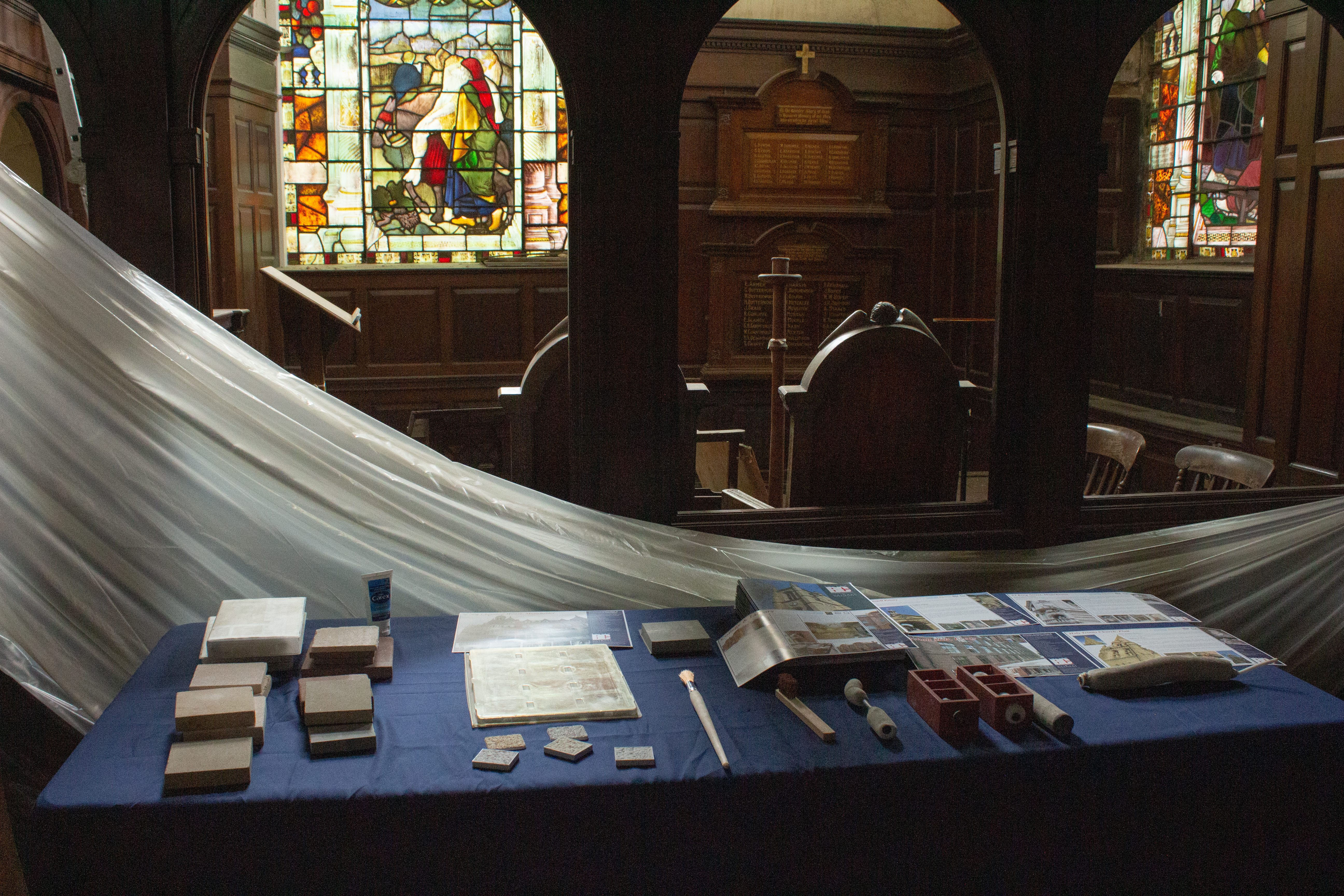 Interior of St.Johns during summer school showing two stained glass windows in the background and a table with traditional craft tools display in the foreground.